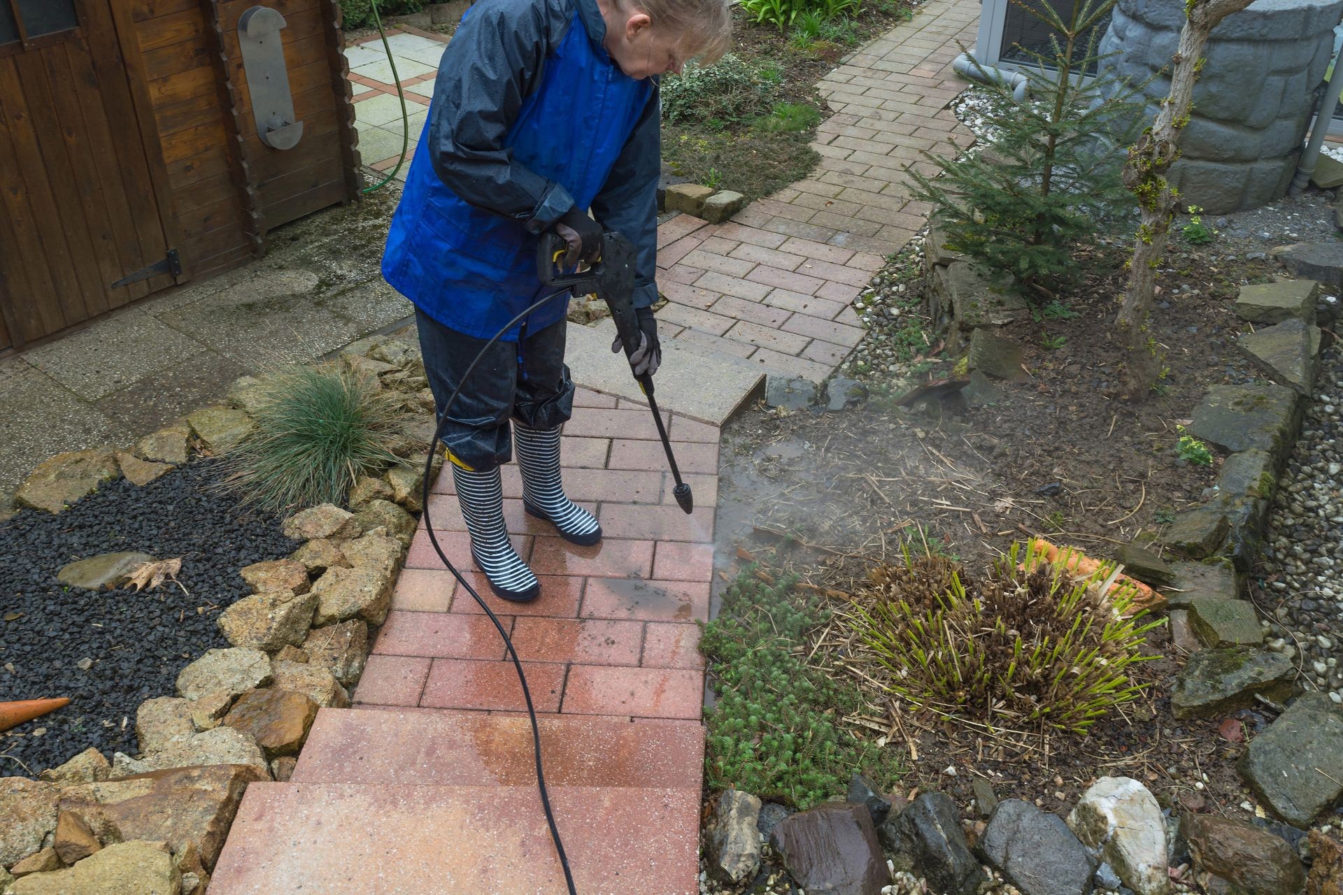 Woman cleans stone slabs with a pressure washer